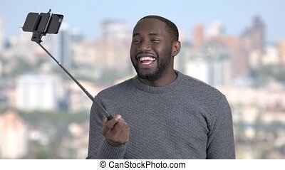Funny african-american guy using selfie stick. young attractive  dark-skinnes man taking selfie with monopod on blurred | CanStock